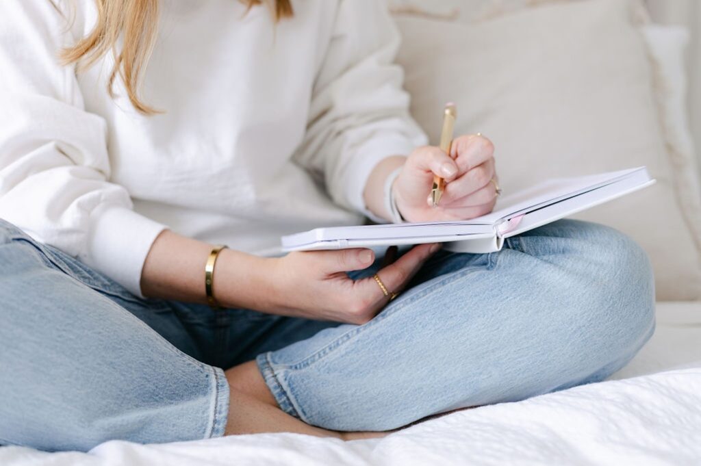 The Perfectionism Therapist, Natalie Englander, a woman sitting on her bed writing with journal prompts for perfectionists to change her inner critic
